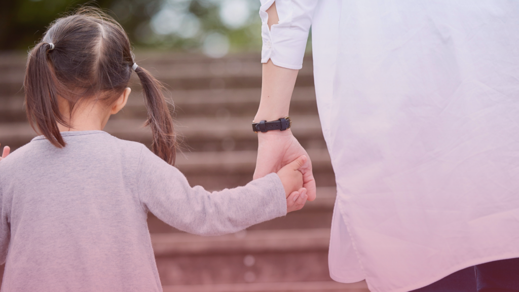 A child and parent holding hands from behind.
